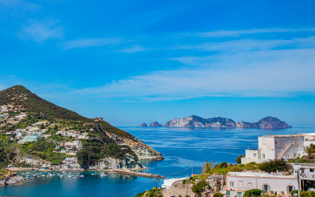 Vista panoramica dell’isola di Ponza con le sue case bianche, il mare blu intenso e l'Isola di Palmarola sullo sfondo.